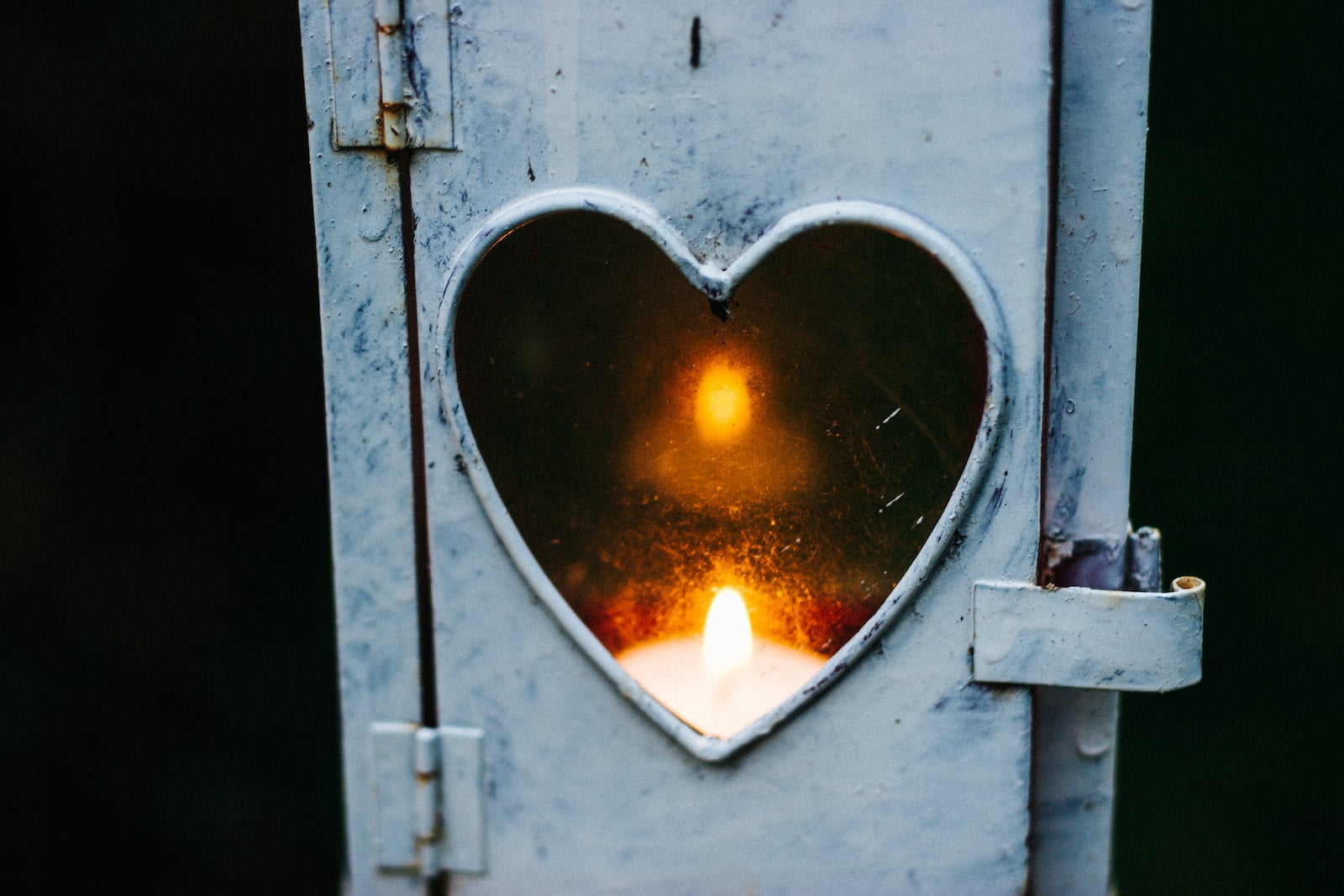 Candle shining through heart-shaped window. Photo credit: Cathal Mac an Bheatha on Unsplash.